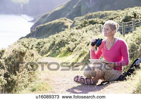 Stock Image - Woman on cliffside path using binoculars. Fotosearch