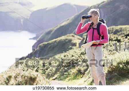Stock Photography - Woman on cliffside path using binoculars. Fotosearch