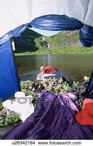 Picture - Woman outdoors at campsite by tent splashing water from river on face. Fotosearch