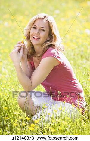 Stock Image - Woman outdoors holding flower smiling. Fotosearch