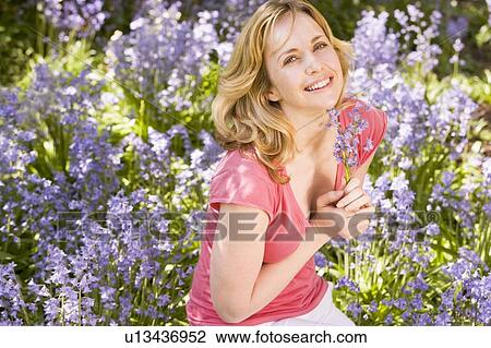 Stock Image - Woman outdoors holding flowers smiling. Fotosearch