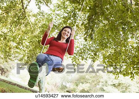 Woman outdoors on tree swing smiling (high key/selective focus) View Large Photo Image Stock Photo - Woman outdoors on tree swing smiling (high key/selective focus). Fotosearch