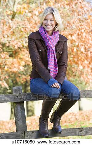 Woman outdoors sitting on fence smiling (selective focus) View Large Photo Image Stock Image - Woman outdoors sitting on fence smiling (selective focus). Fotosearch