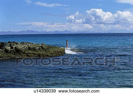 Stock Photo - Woman outdoors standing on large rocks Oceanside (far away). Fotosearch