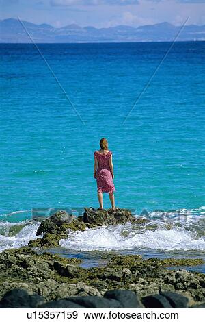 Stock Photo - Woman outdoors standing on large rocks by the ocean. Fotosearch