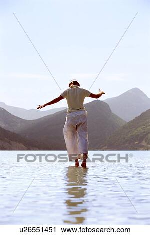 Stock Image - Woman outdoors walking on water in scenic location. Fotosearch