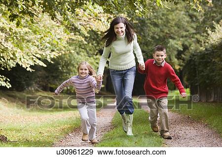 Woman outdoors with two young children walking on path holding hands and smiling (selective focus) View Large Photo Image Stock Photo - Woman outdoors with two young children walking on path holding hands and smiling (selective focus). Fotosearch
