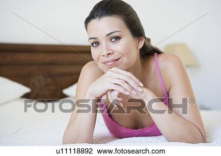 Stock Image - Woman relaxing on bed in bedroom smiling (selective focus). Fotosearch