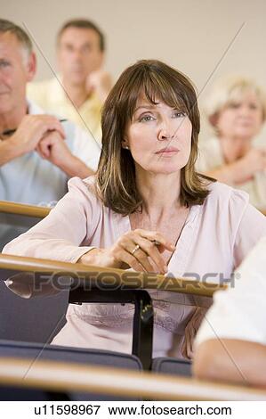 Woman sitting in adult classroom with students in background (selective focus) View Large Photo Image Stock Photo - Woman sitting in adult classroom with students in background (selective focus). Fotosearch