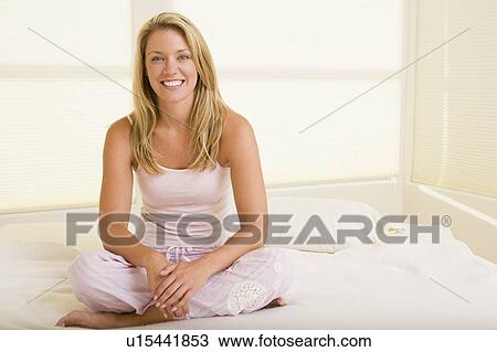 Stock Image - Woman sitting in bedroom smiling. Fotosearch