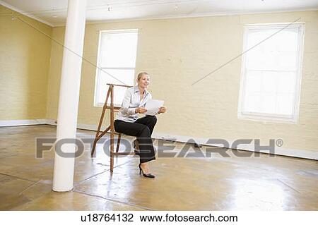 Woman sitting on ladder in empty space holding paper smiling View Large Photo Image Stock Image - Woman sitting on ladder in empty space holding paper smiling. Fotosearch