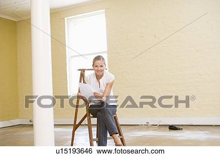 Stock Photograph - Woman sitting on ladder in empty space holding paper. Fotosearch