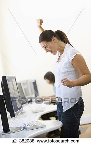 Stock Photo - Woman standing in computer room cheering and smiling. Fotosearch