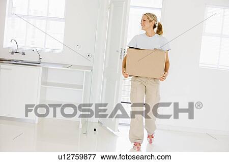 Stock Photo - Woman with box moving into new home smiling. Fotosearch