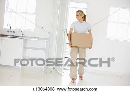 Stock Photo - Woman with box moving into new home smiling. Fotosearch