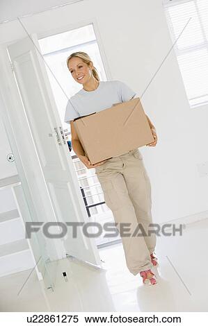 Stock Photography - Woman with box moving into new home smiling. Fotosearch