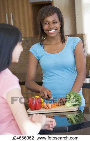 Stock Image - Women Laughing With Friend While Preparing meal, mealtime. Fotosearch