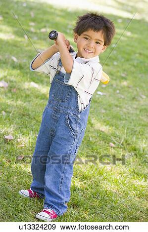 Stock Photo - Young boy holding baseball bat outdoors smiling. Fotosearch