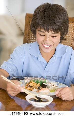 Stock Image - Young boy in dining room eating chinese food smiling. Fotosearch