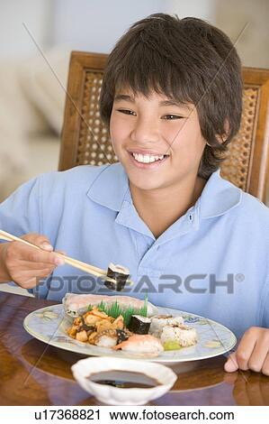 Stock Image - Young boy in dining room eating chinese food smiling. Fotosearch