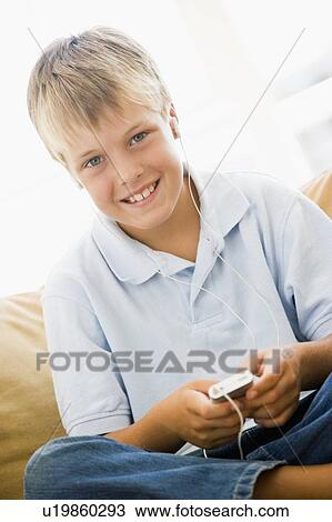 Stock Image - Young boy in living room with MP3 player smiling. Fotosearch