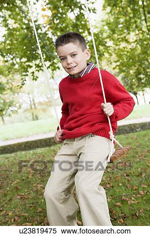 Stock Photography - Young boy outdoors on tree swing smiling (selective focus). Fotosearch
