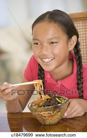 Stock Photo - Young girl in dining room eating chinese food smiling. Fotosearch
