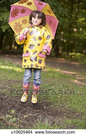 Picture - Young girl outdoors with umbrella jumping and smiling. Fotosearch