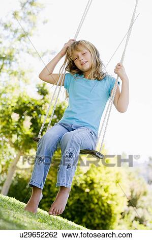 Stock Image - Young girl sitting on swing smiling. Fotosearch