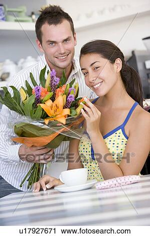 Young man giving a bouquet of flowers to a young girl sitting at a table View Large Photo Image Stock Image - Young man giving a bouquet of flowers to a young girl sitting at a table. Fotosearch