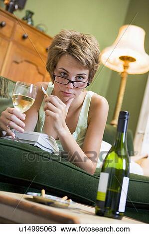 Stock Image - Young woman at home smoking and drinking wine by telephone. Fotosearch
