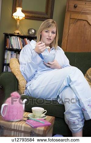 Young woman lying on sofa at home eating a sweet treat View Large Photo Image Picture - Young woman lying on sofa at home eating a sweet treat. Fotosearch