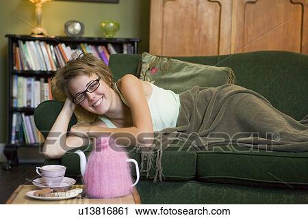 Stock Image - Young woman lying on sofa at home. Fotosearch