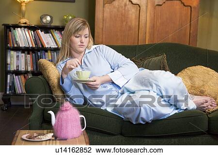 Young woman lying on sofa at home drinking tea View Large Photo Image Stock Image - Young woman lying on sofa at home drinking tea. Fotosearch