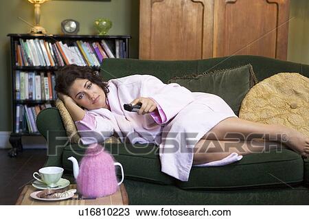 Young woman lying on sofa at home watching television View Large Photo Image Stock Image - Young woman lying on sofa at home watching television. Fotosearch
