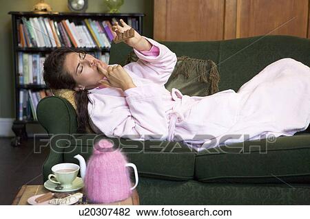Young woman lying on sofa at home eating chocolate View Large Photo Image Stock Image - Young woman lying on sofa at home eating chocolate. Fotosearch