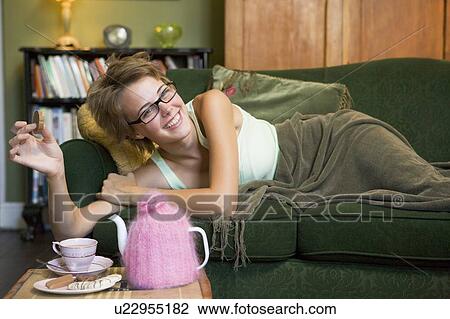 Young woman lying on sofa at home eating cookies and drinking tea View Large Photo Image Stock Image - Young woman lying on sofa at home eating cookies and drinking tea. Fotosearch