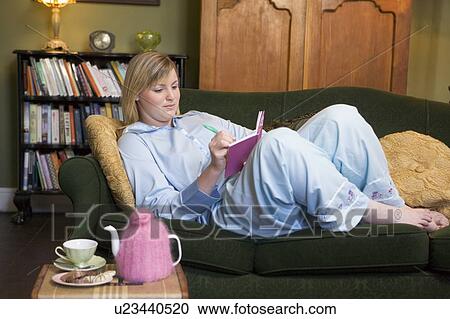 Young woman lying on sofa at home writing in her diary View Large Photo Image Stock Image - Young woman lying on sofa at home writing in her diary. Fotosearch
