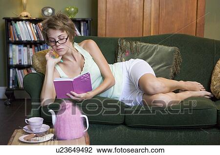 Stock Image - Young woman lying on sofa at home writing in her diary. Fotosearch
