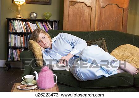 Stock Image - Young woman lying on sofa at home waiting by telephone. Fotosearch
