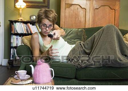 Stock Photo - Young woman lying on sofa at home watching television. Fotosearch