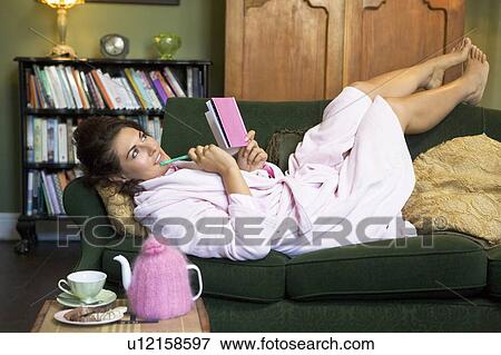 Stock Photo - Young woman lying on sofa at home writing in her diary. Fotosearch