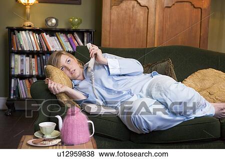 Young woman lying on sofa at home holding telephone View Large Photo Image Stock Photo - Young woman lying on sofa at home holding telephone. Fotosearch
