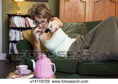 Young woman lying on sofa at home eating cookies and watching television View Large Photo Image Stock Photo - Young woman lying on sofa at home eating cookies and watching television. Fotosearch