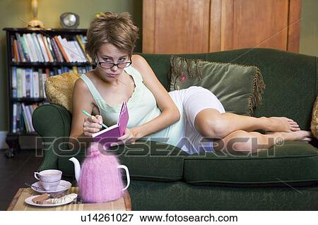 Young woman lying on sofa at home writing in her diary View Large Photo Image Stock Photo - Young woman lying on sofa at home writing in her diary. Fotosearch