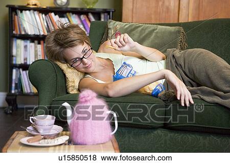 Stock Photo - Young woman lying on sofa at home eating potato chips. Fotosearch