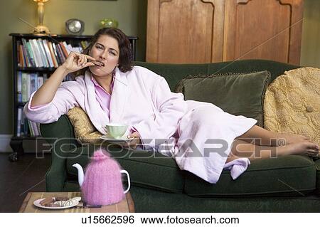 Young woman lying on sofa at home eating cookies and drinking tea View Large Photo Image Stock Photograph - Young woman lying on sofa at home eating cookies and drinking tea. Fotosearch