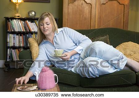 Young woman lying on sofa at home eating cookies and drinking tea View Large Photo Image Stock Photography - Young woman lying on sofa at home eating cookies and drinking tea. Fotosearch