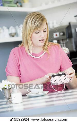 Picture - Young woman sitting at a table checking change purse. Fotosearch