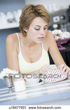 Stock Image - Young woman sitting at a table checking change purse. Fotosearch